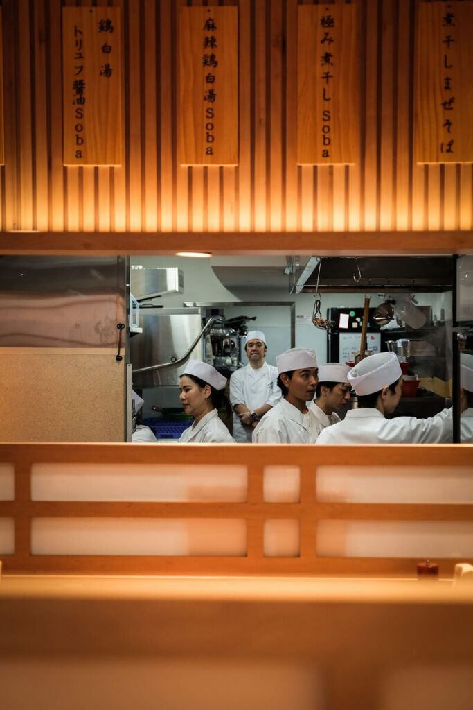 Chefs at work in the Ginza Kagari kitchen, seen through the pass beneath the hanging menu boards