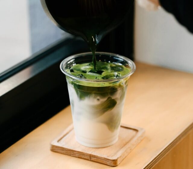 Matcha being poured over iced milk in a takeaway cup