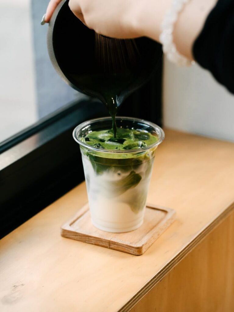 Matcha being poured over iced milk in a takeaway cup