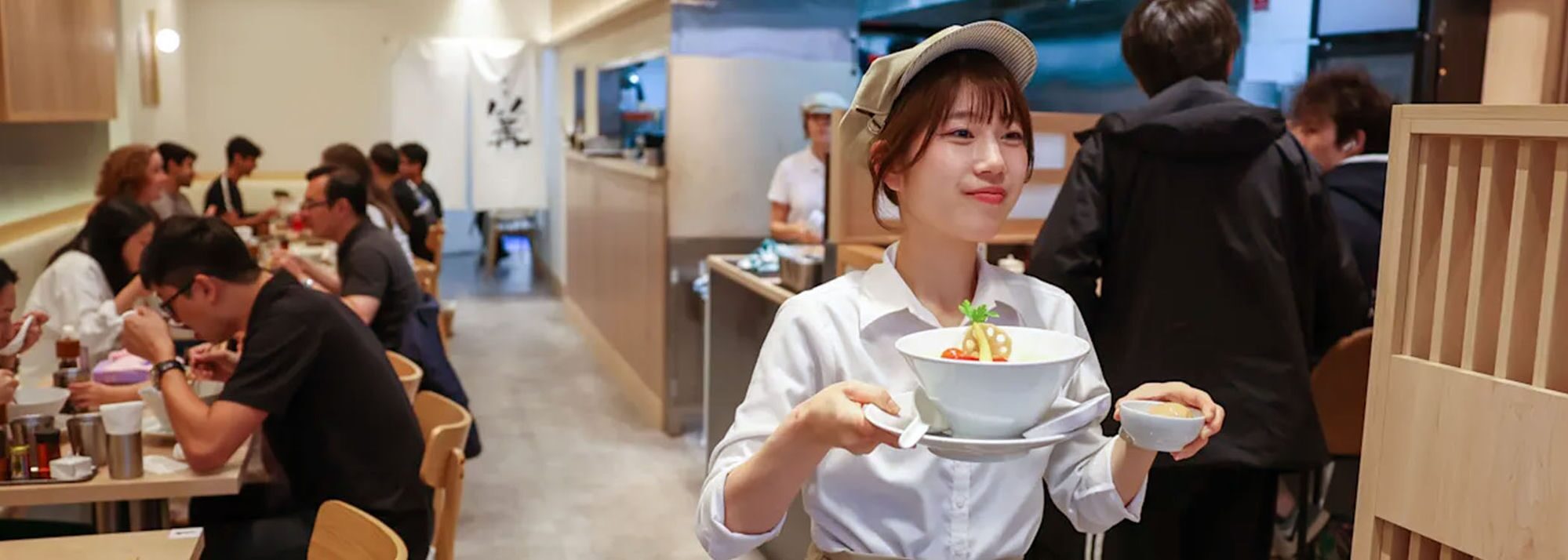 A Ginza Kagari server carrying a bowl of ramen through the dining room